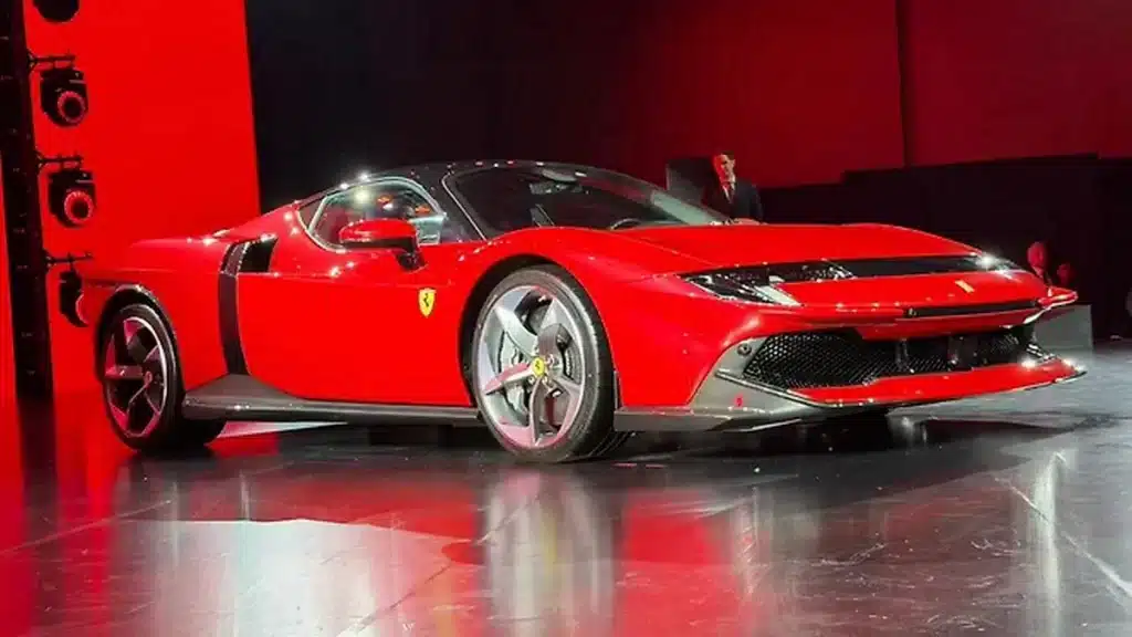 Ferrari 849 Testarossa: ભારતમાં લોન્ચ થઈ ફેરારીની સૌથી શક્તિશાળી સુપરકાર, જાણો કિંમત અને ફીચર્સ. 2 સ્ટેજ પર લાલ રંગની ફેરારી 849 ટેસ્ટારોસા, જે તેની આધુનિક હેડલાઇટ્સ અને એરોડાયનેમિક આકાર દર્શાવે છે.